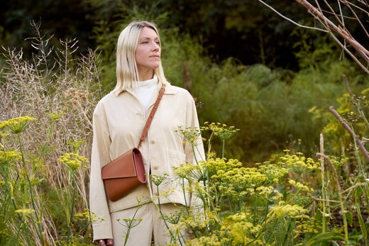 CARV founder Becky standing in amongst flowers wearing a crossbody tan leather bag