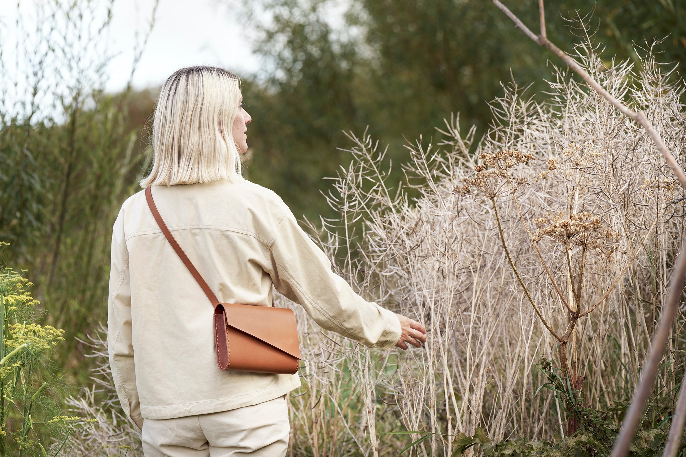 Becky from CARV stood among plants wearing a tan leather crossbody bag