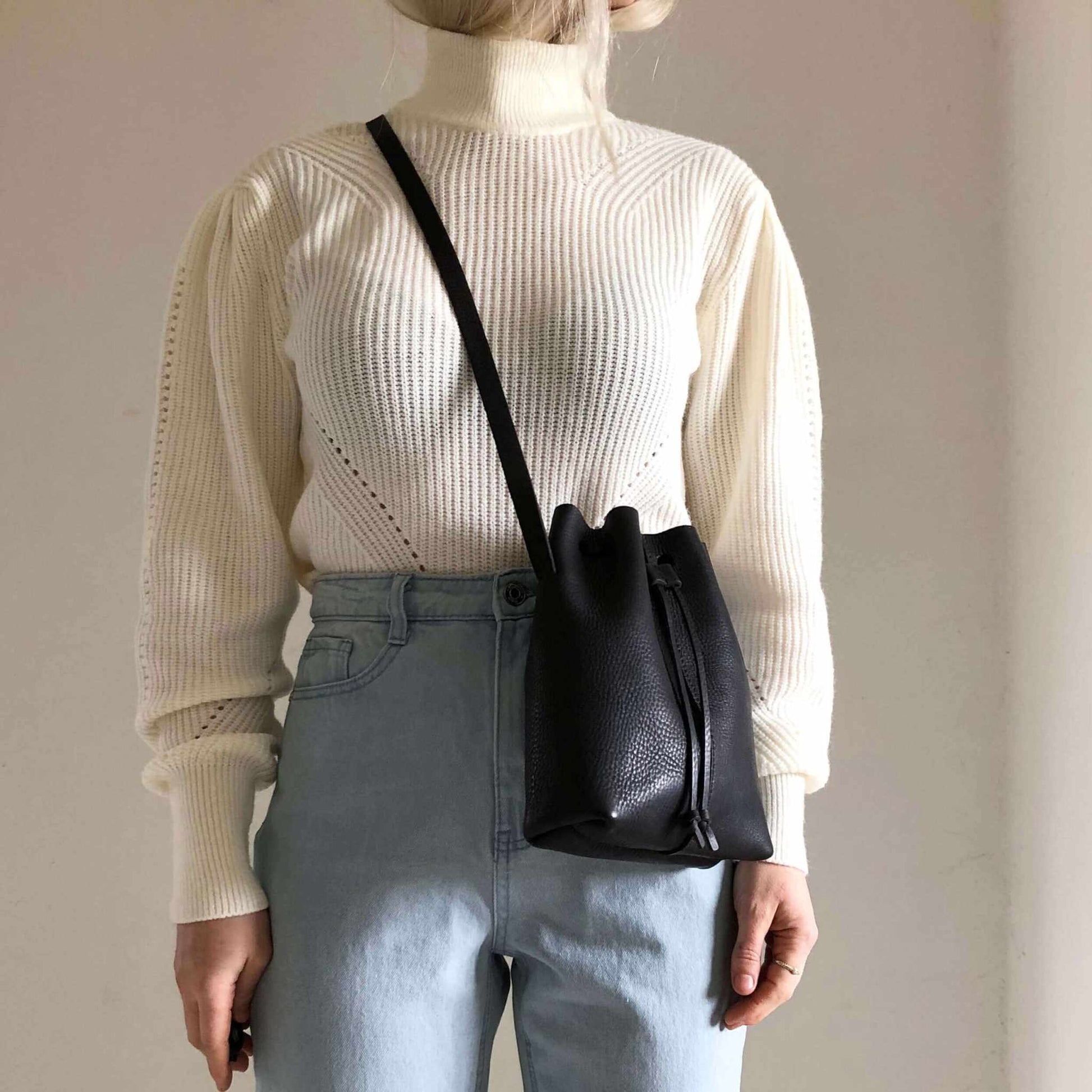 Nomad Mini Leather Bucket Bag crossbody in black, worn with a white sweater and blue jeans.