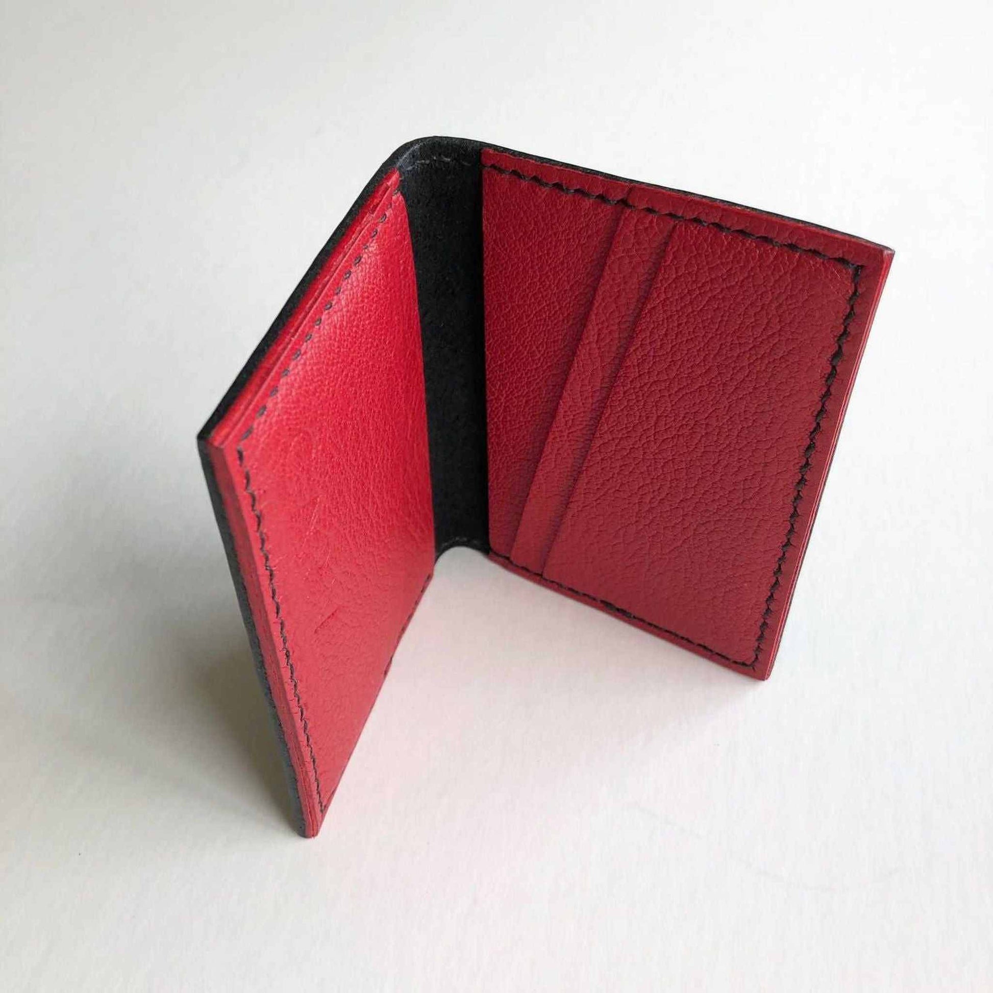 Hand stitched black leather bifold card wallet with red interior slots.