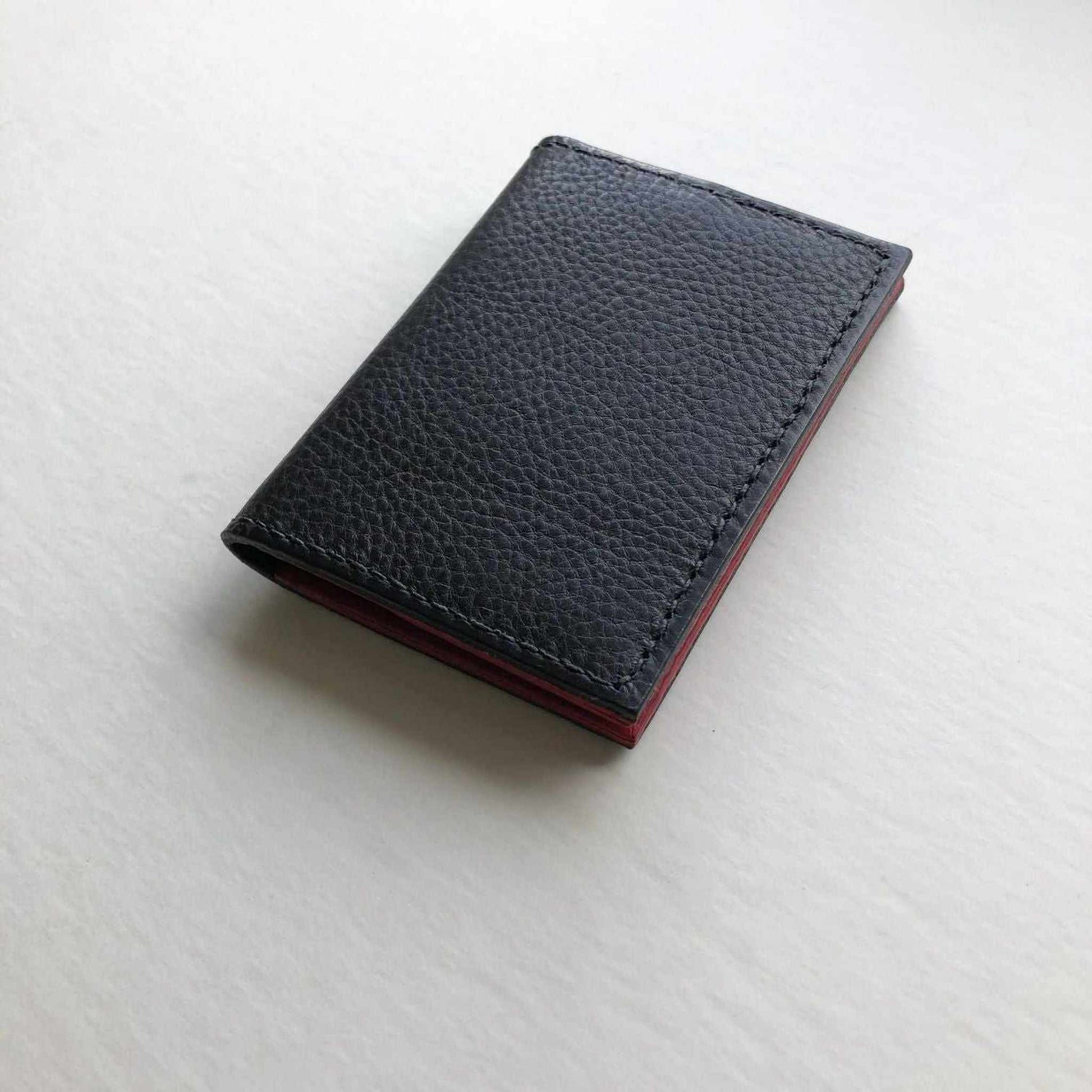 Hand stitched black leather bifold card wallet with pebble texture and red accent stitching.