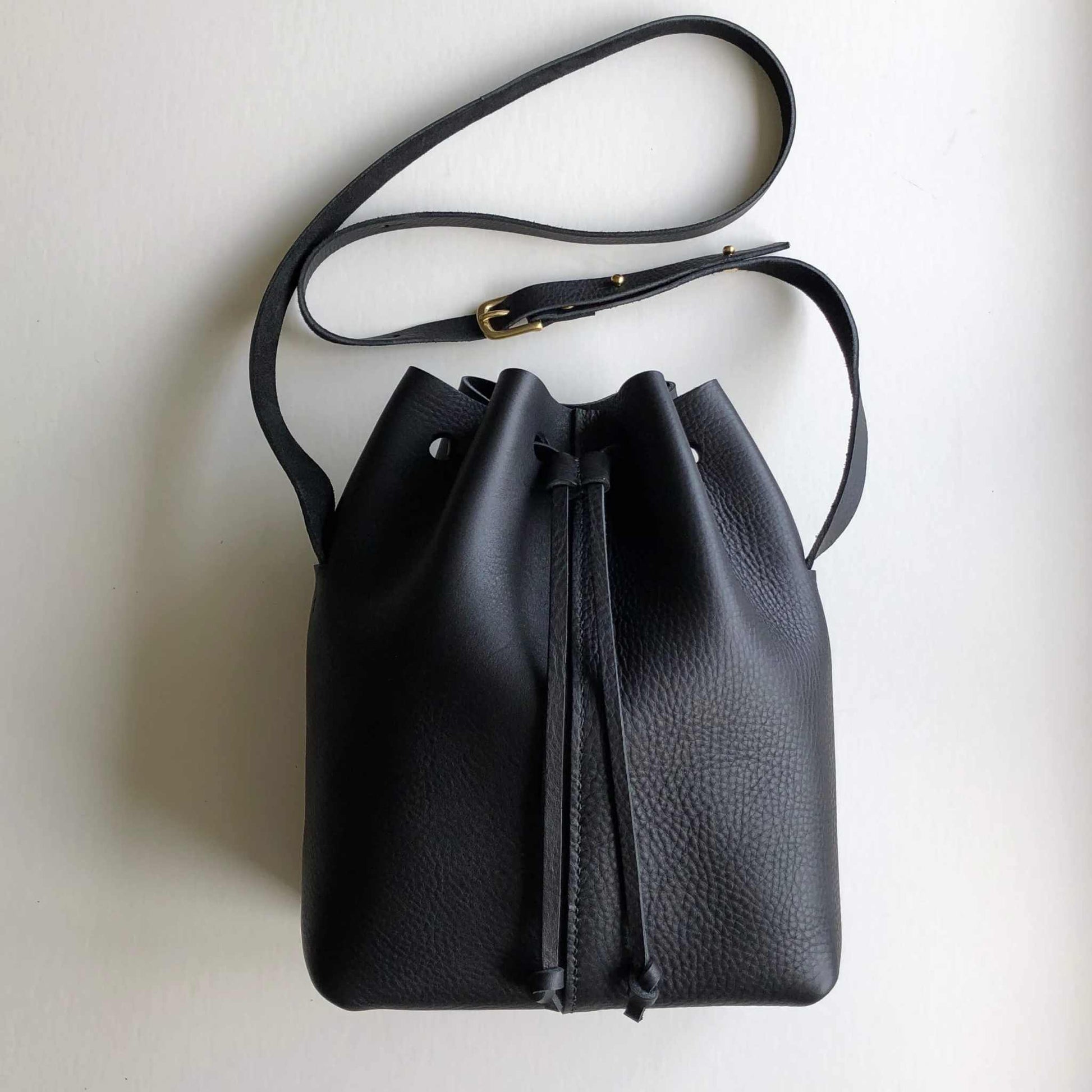 Nomad Midi Black Leather Bucket Bag with adjustable strap and drawstring closure.