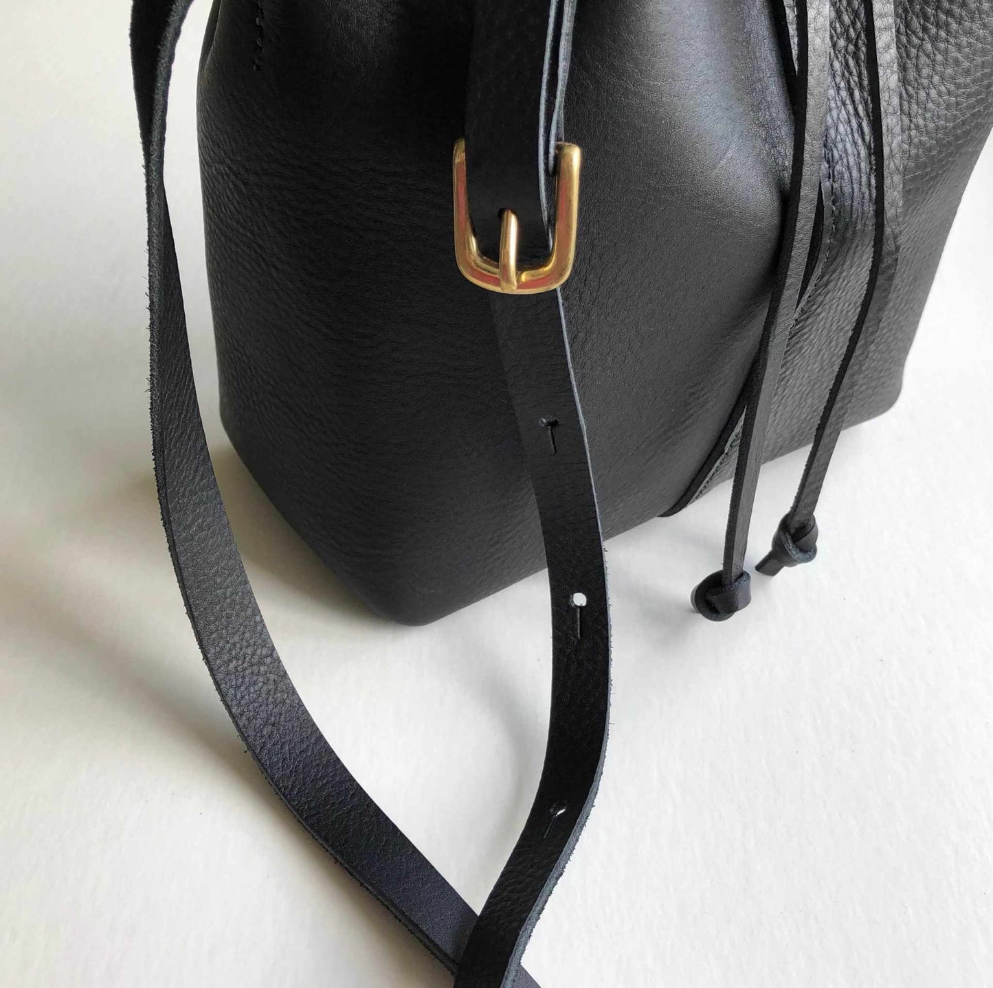 Nomad Midi Black Leather Bucket Bag with adjustable strap and drawstring detail, handcrafted in the UK.