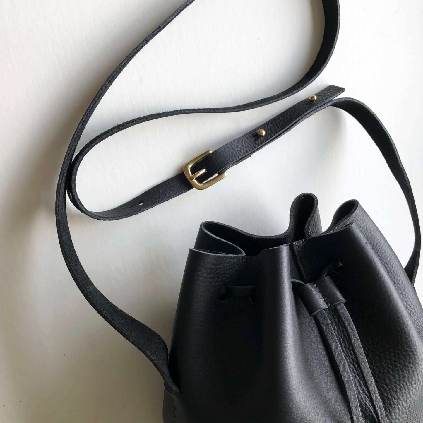 Nomad Midi Black Leather Bucket Bag with adjustable shoulder strap and drawstring closure, handcrafted with sustainably sourced leather.