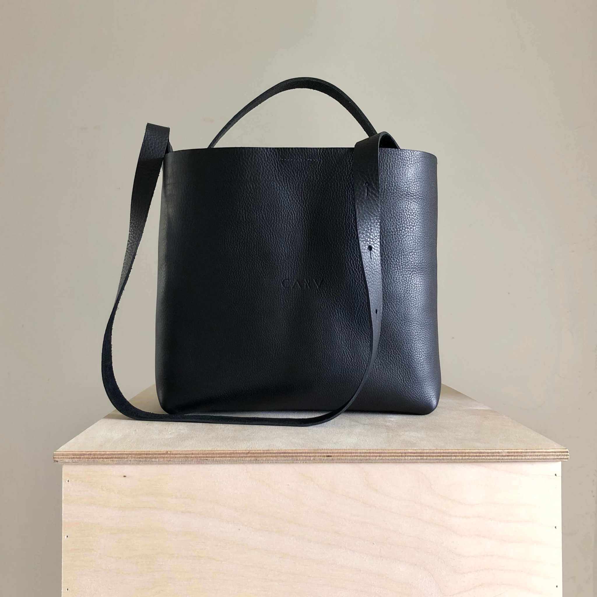 Basket Midi Leather Tote Bag in black leather displayed on a stand.