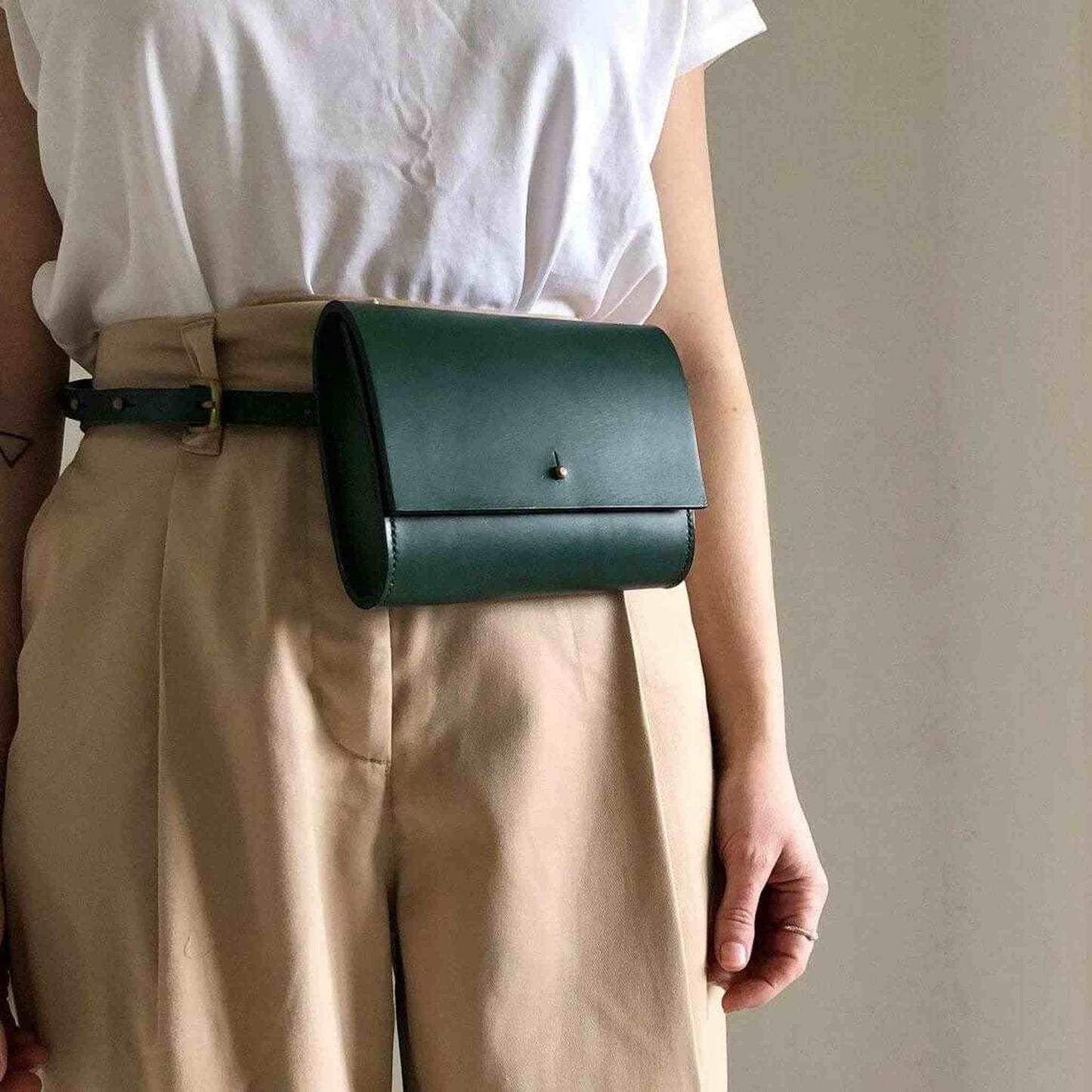 Sedna green leather belt bag worn around waist, minimalist design.