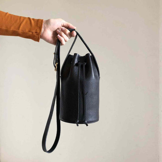 Cylinder Mini Leather Bucket Bag in black with adjustable strap, timeless craftsmanship, minimalist design, elegant and sustainable accessory.