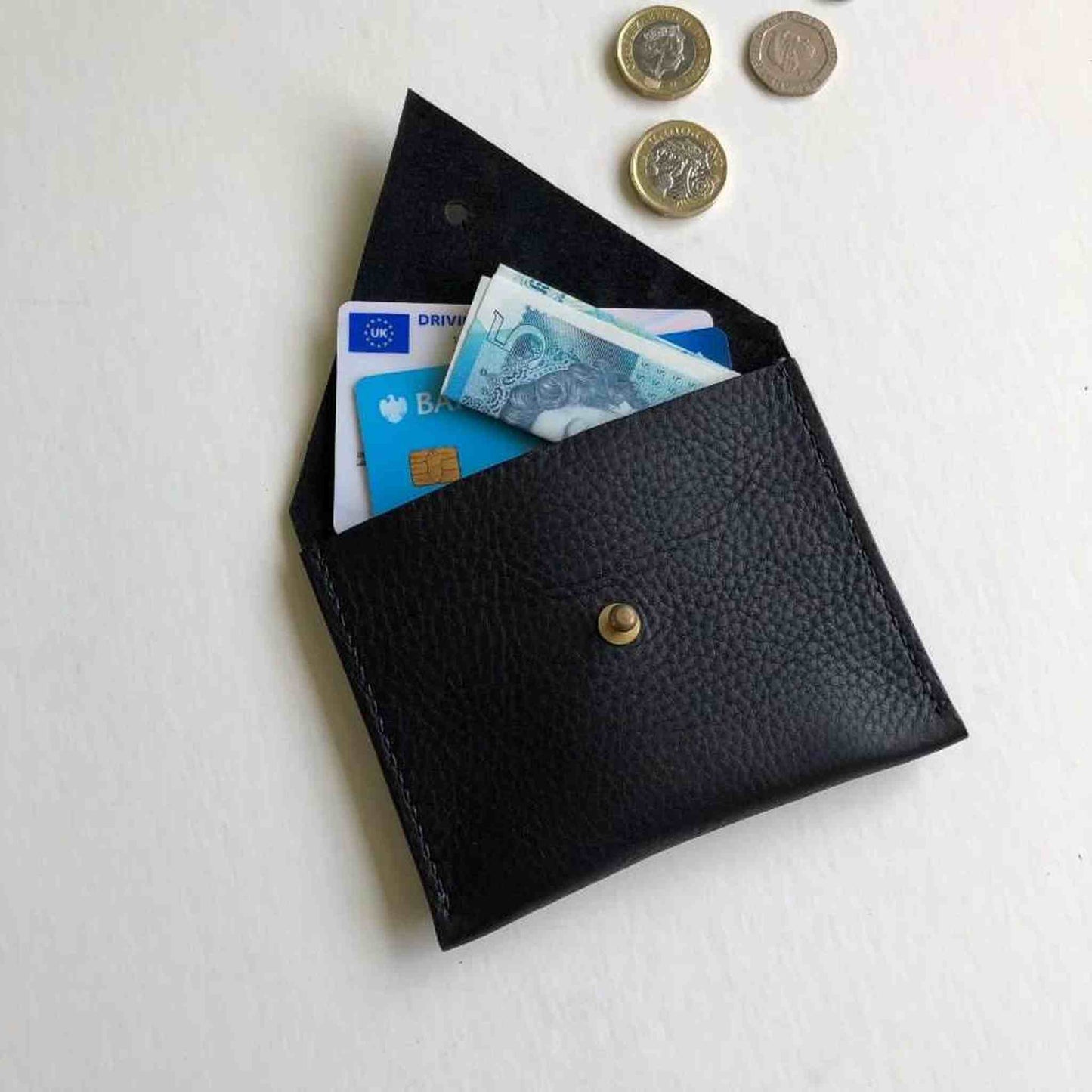 Black leather coin purse with triangle flap, brass stud closure, holding cards and banknotes.