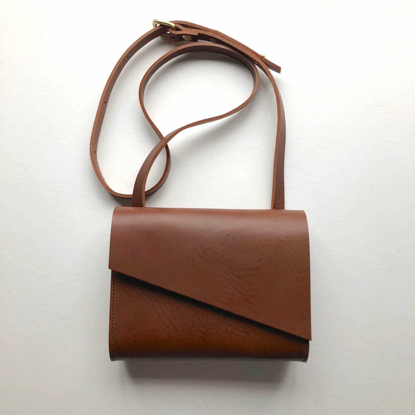 Tan leather crossbody bag with adjustable strap and minimalist design.