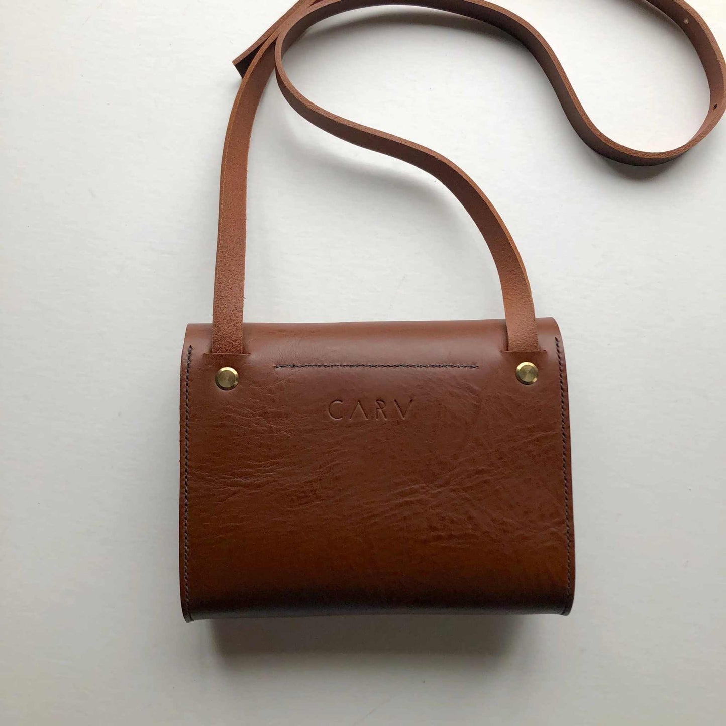 Tan leather crossbody bag with adjustable strap and handcrafted detailing.