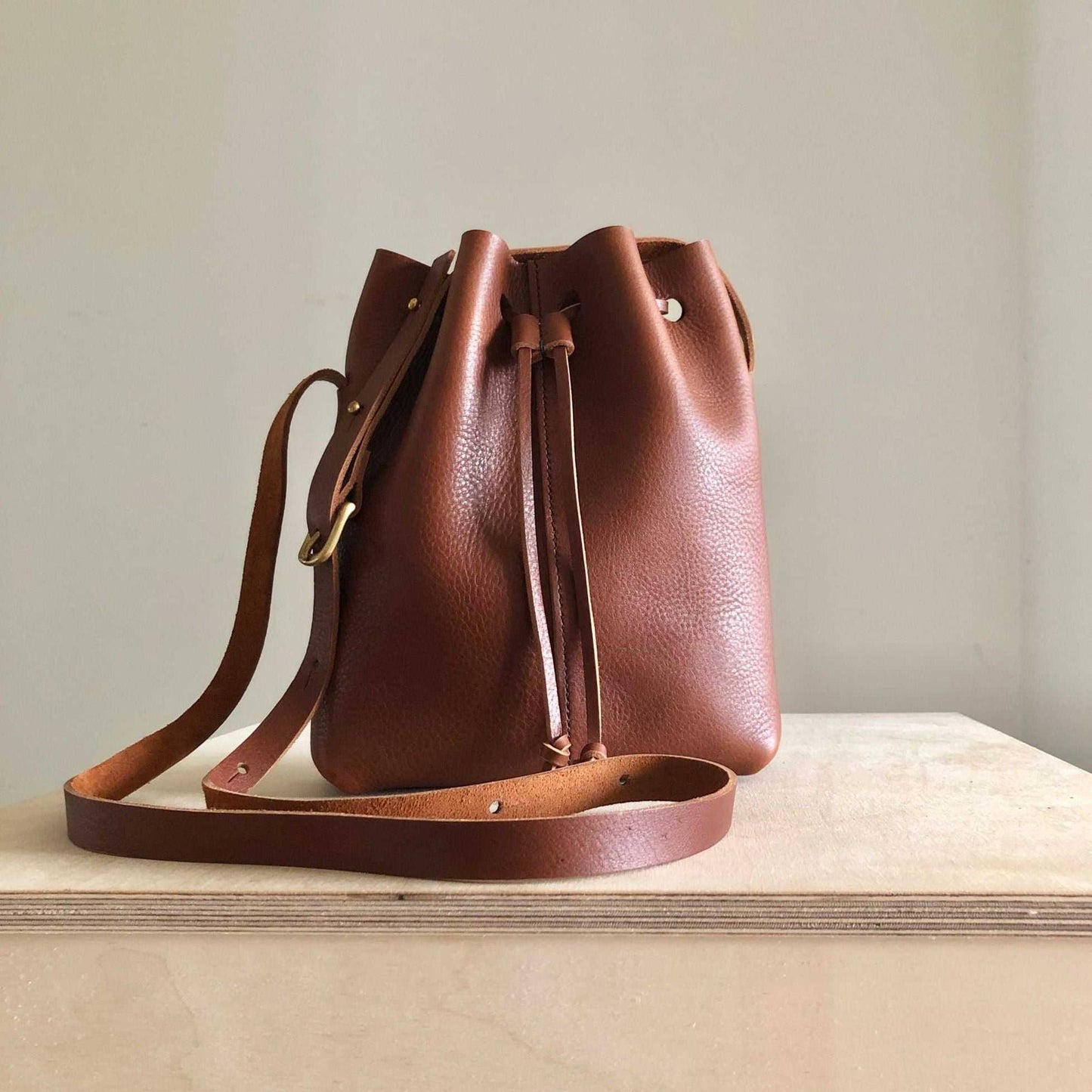 Nomad Mini Leather Bucket Bag in tan brown leather with adjustable strap and brass buckle, handcrafted in the UK.