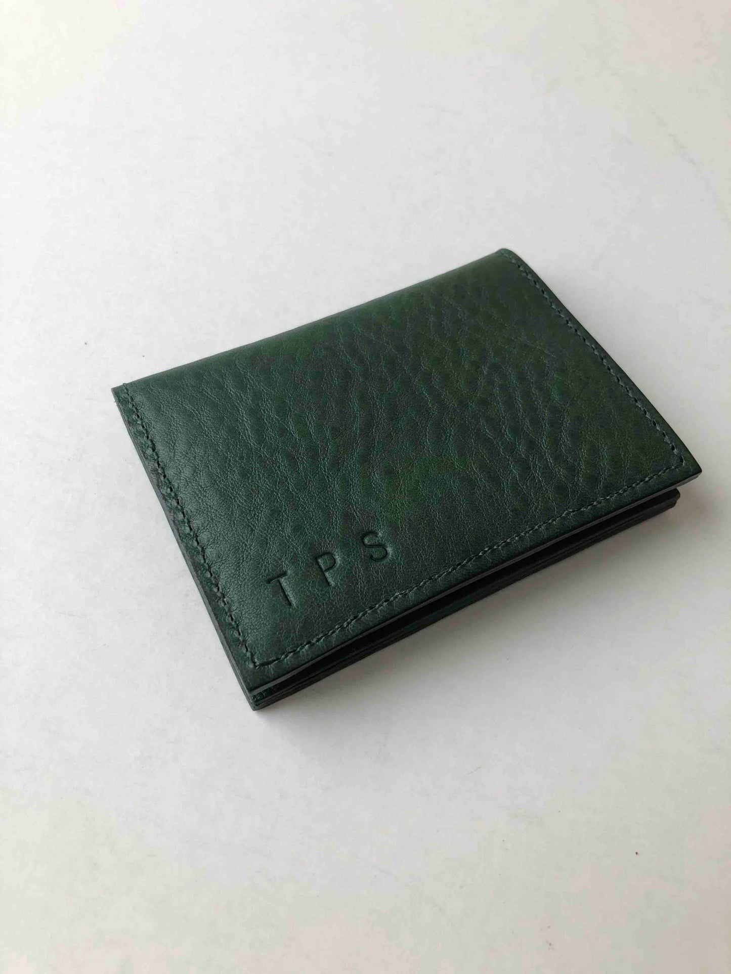 Personalised green leather card wallet with embossed initials, featuring a raised grain pebble design.