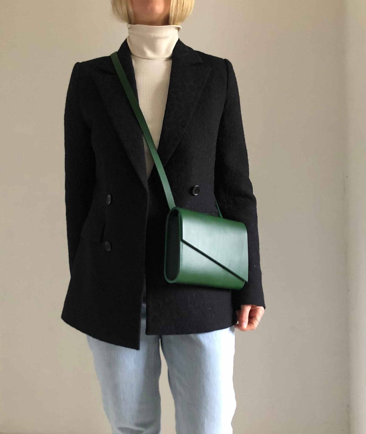 Mini green leather crossbody bag worn with black coat and jeans.