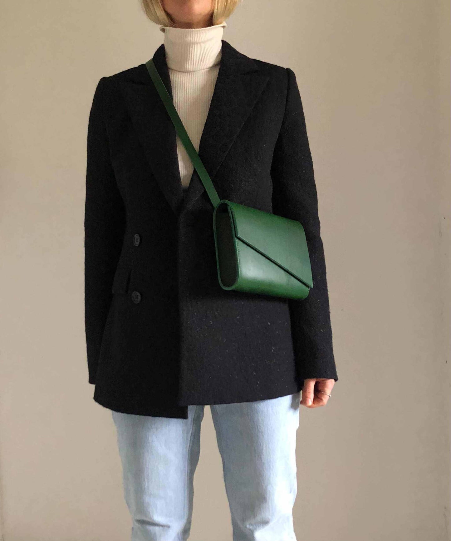 Green leather crossbody bag worn with a black coat and jeans.