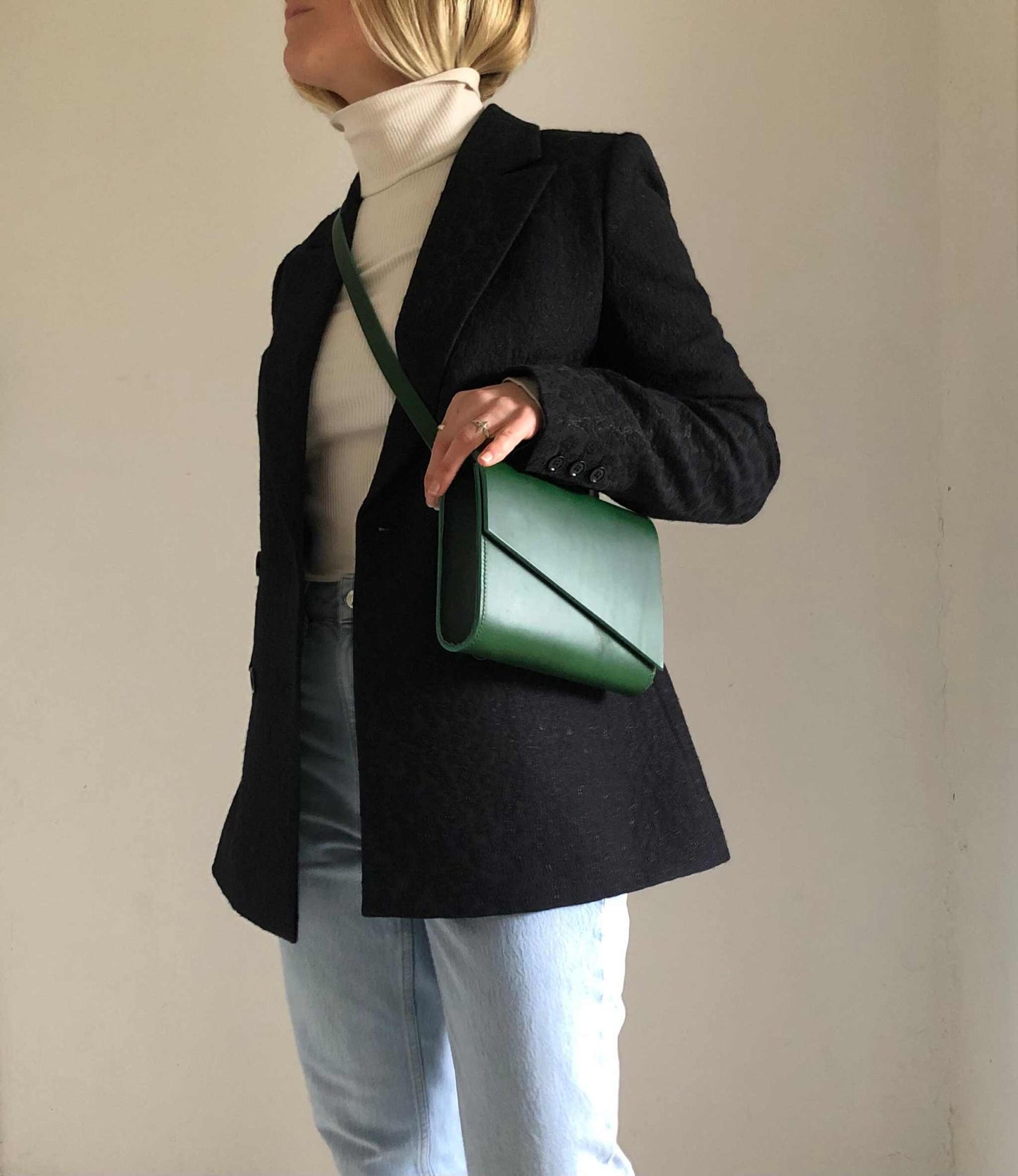 Green leather crossbody bag worn over black coat and jeans, stylish and minimalist accessory.