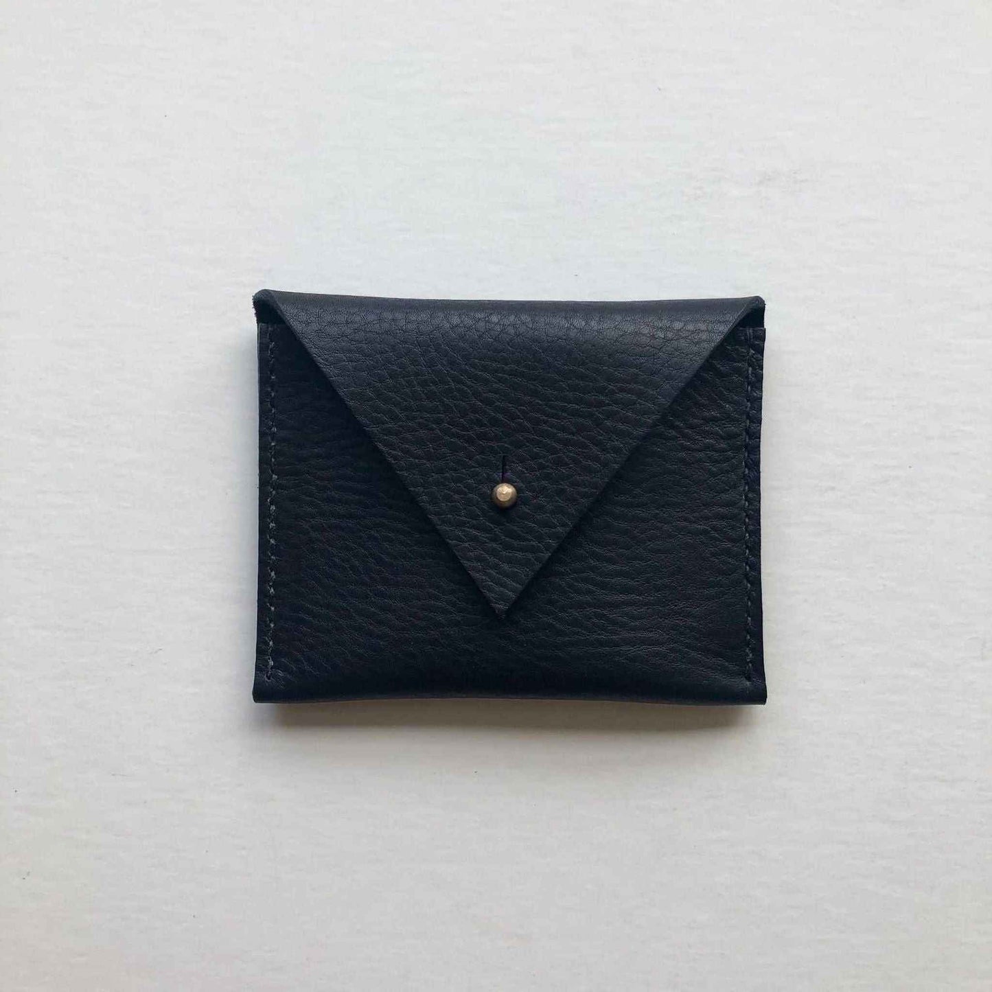 Black leather coin purse with triangle flap and brass closure.