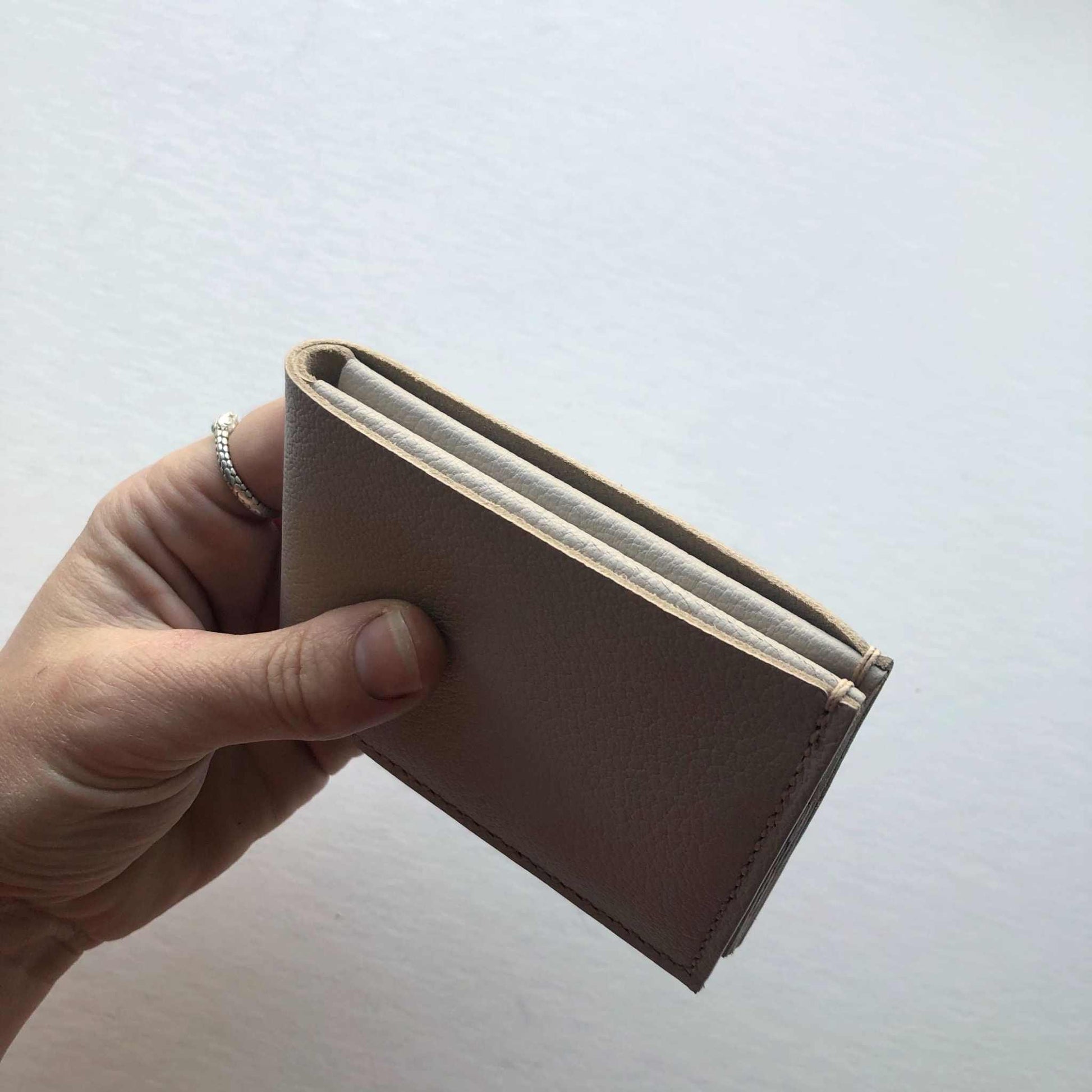 Handmade leather bifold wallet in taupe grey held by a hand, showcasing minimalist design and craftsmanship.