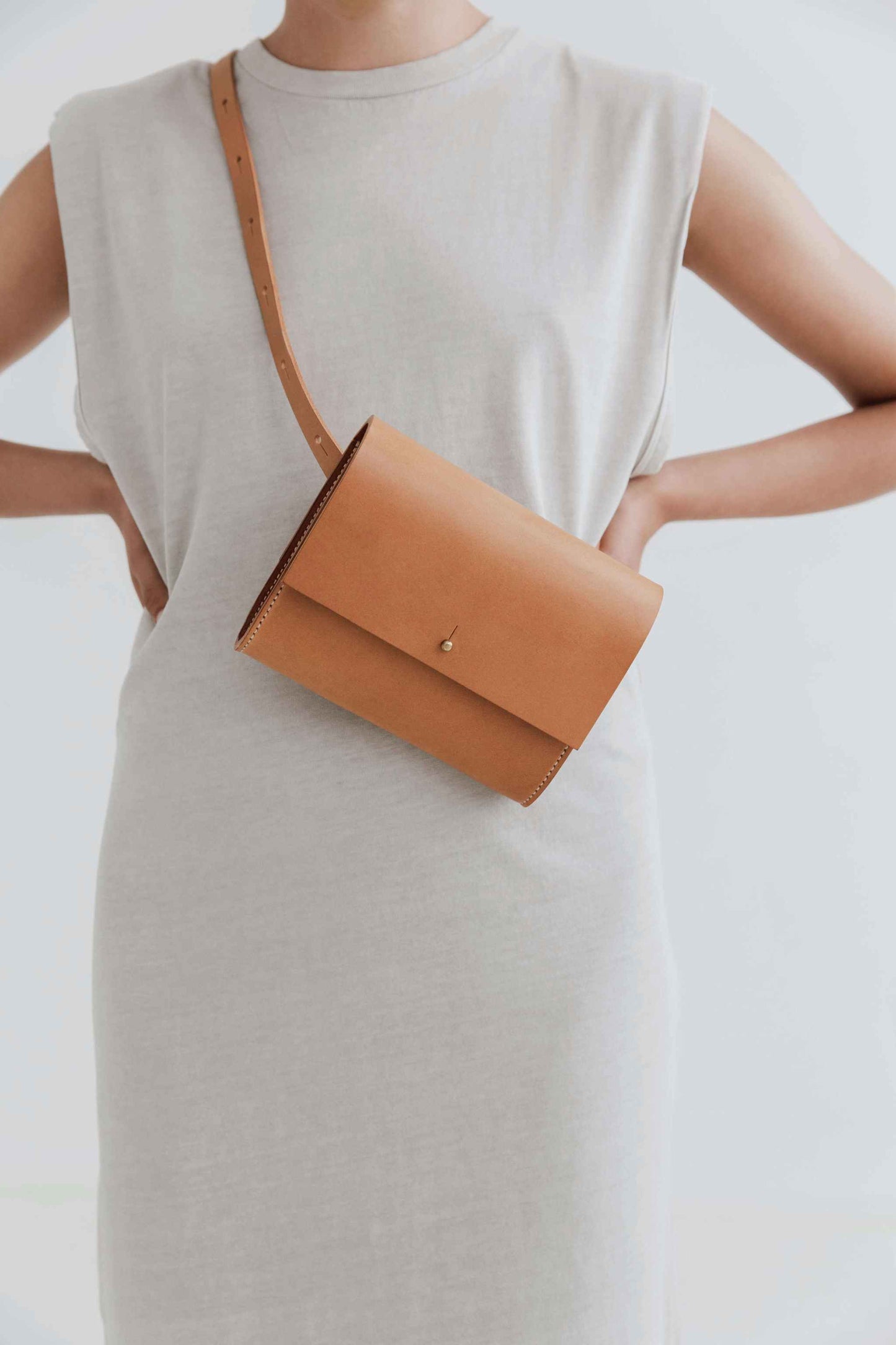 Tan leather belt bag worn crossbody on a woman in a white dress.