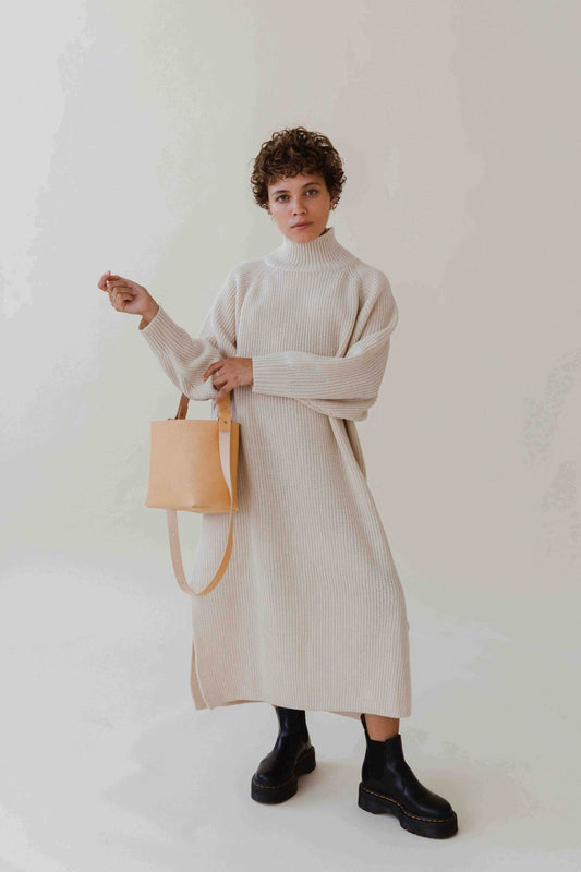 Basket Mini Leather Tote Bag in natural color held by model in beige outfit and black boots.