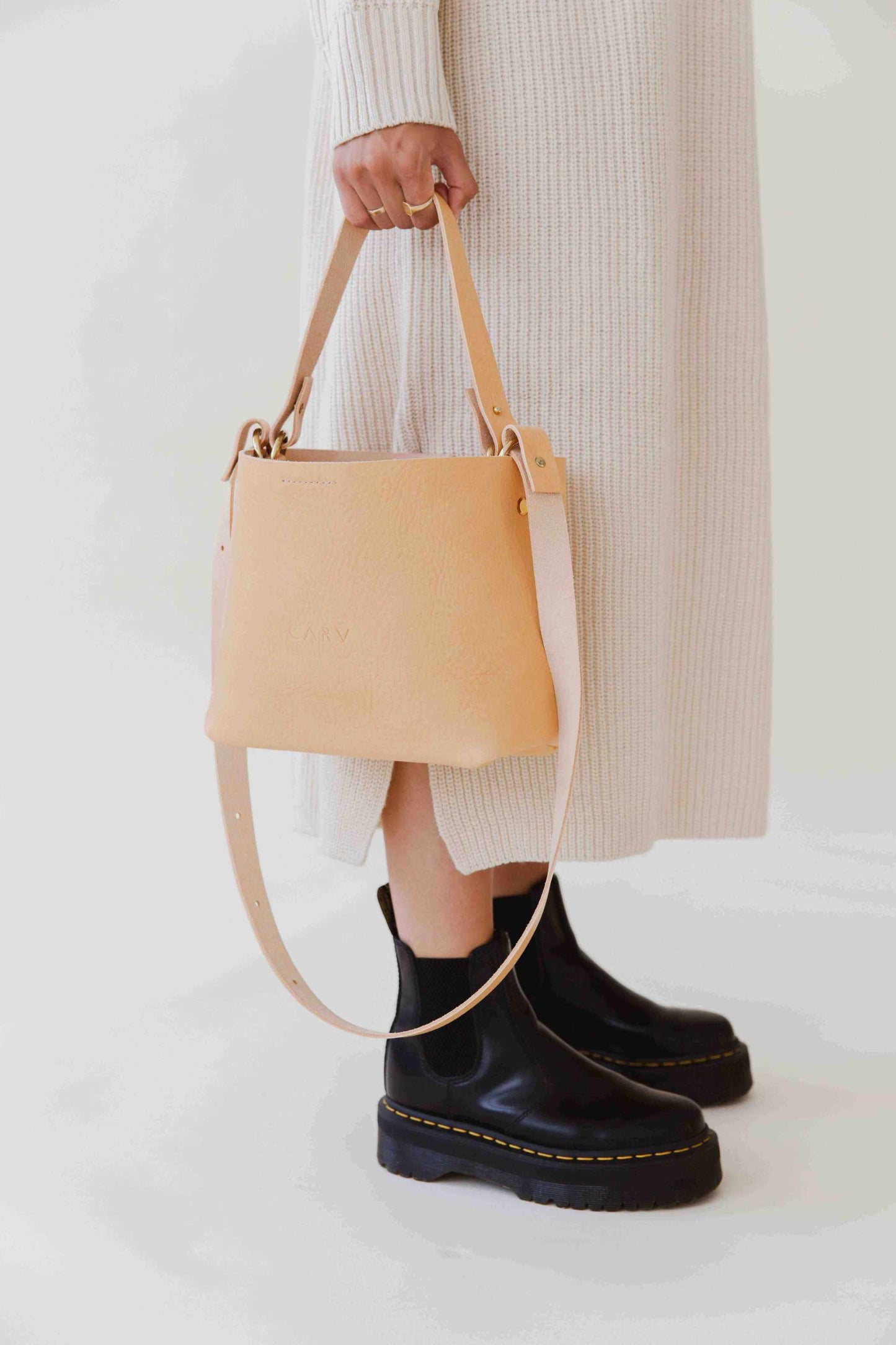 Basket Mini Leather Tote Bag in natural color with adjustable strap, featuring a minimalist design, shown on model wearing black boots.