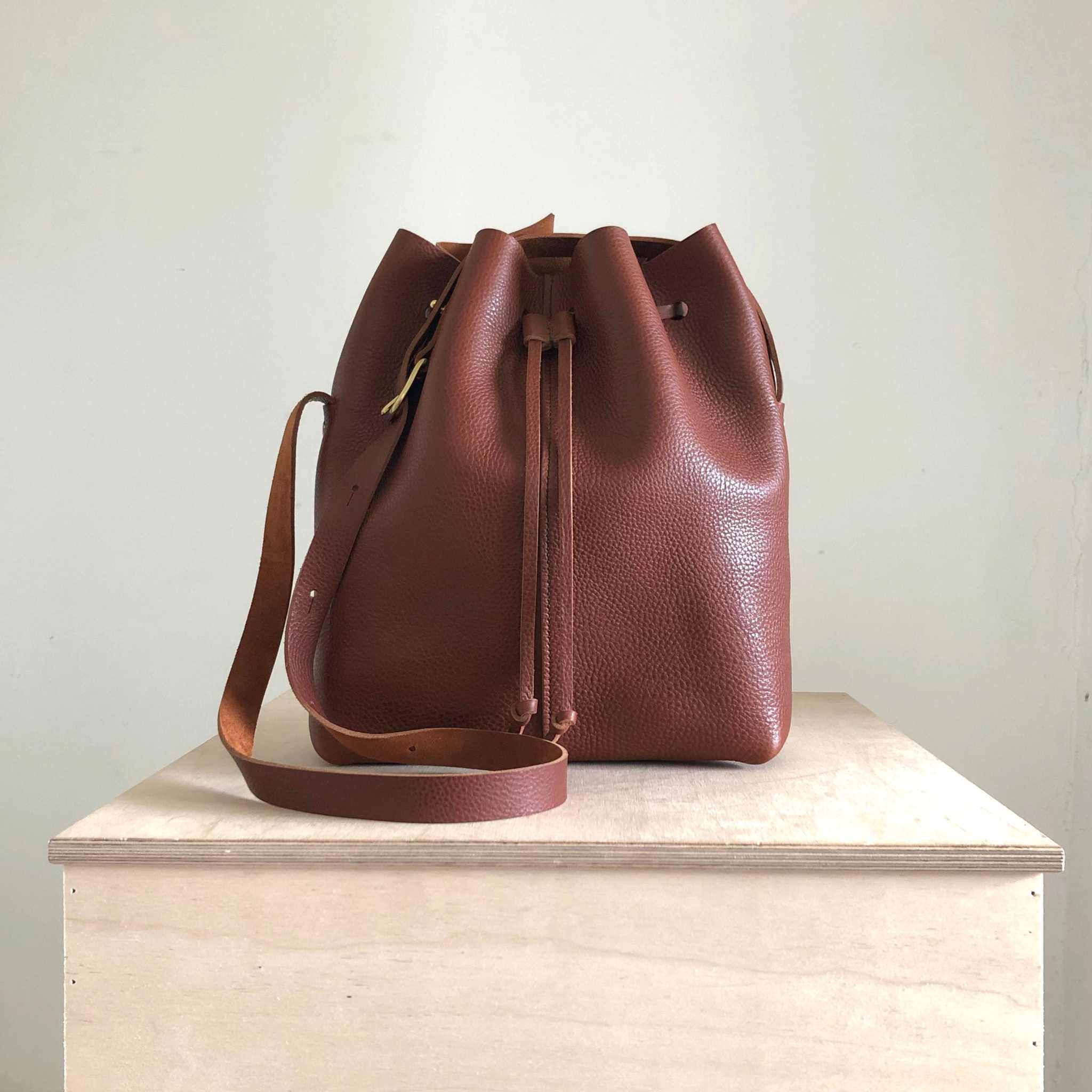 Nomad Maxi Leather Bucket Bag in tan on display surface.