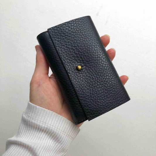 Nomad Mini Handmade Leather Wallet in black, showcasing a pebble texture and brass press stud, held in hand.