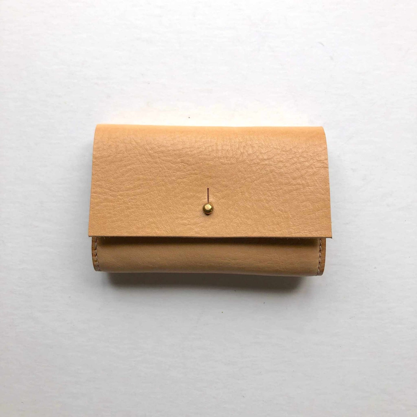 Nomad Mini Handmade Leather Wallet in Nude on white background showing geometric flap and brass press stud.