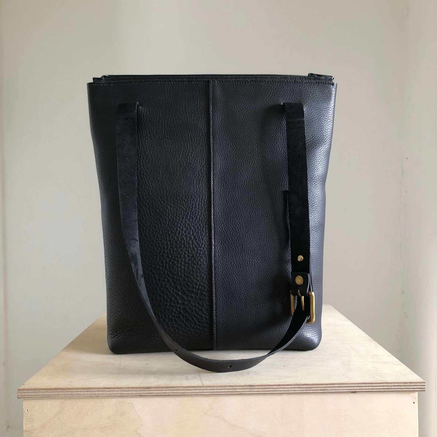 Nomad Black Leather Shopper Bag on wooden surface; minimalist design, handcrafted UK craftsmanship.