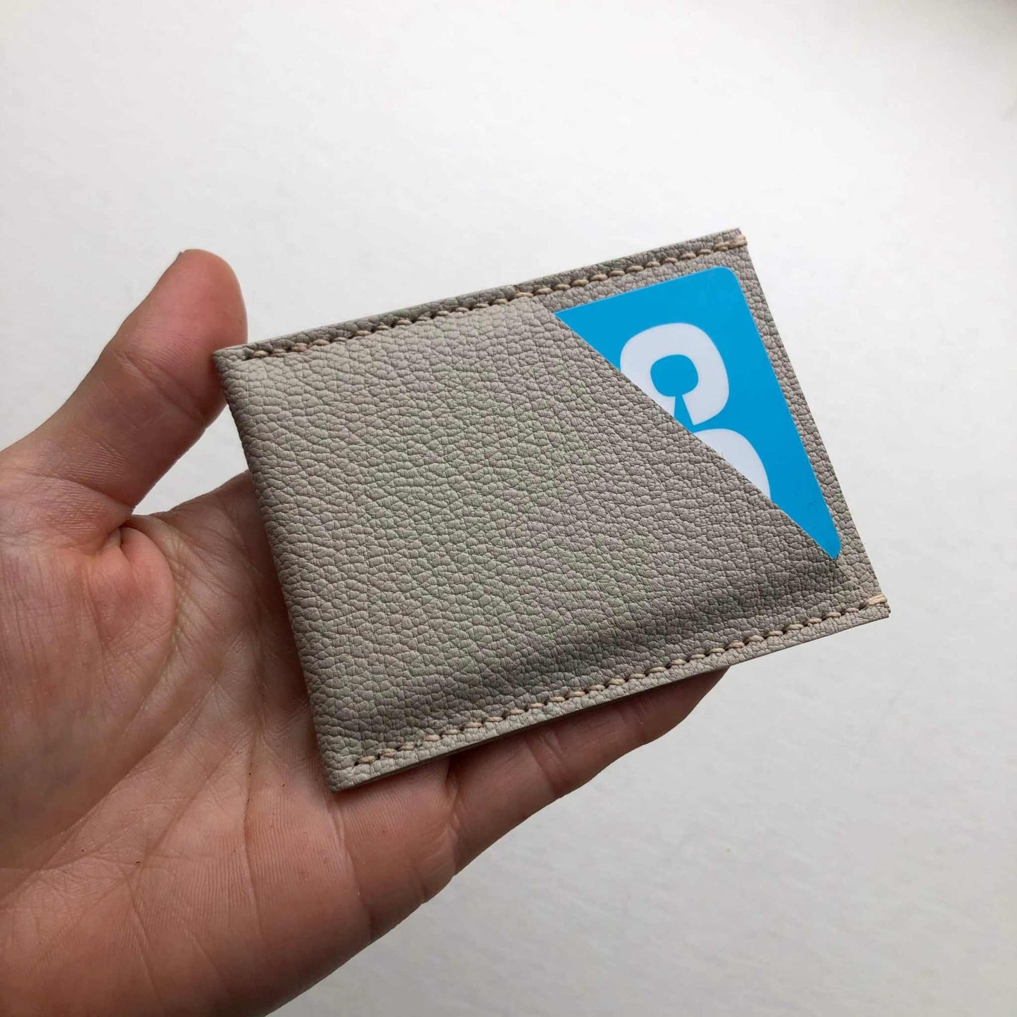 Minimalist taupe leather card sleeve held in hand, showcasing card capacity.