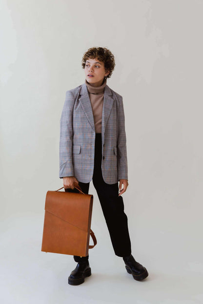 Minimalist tan leather backpack held by person in stylish attire.