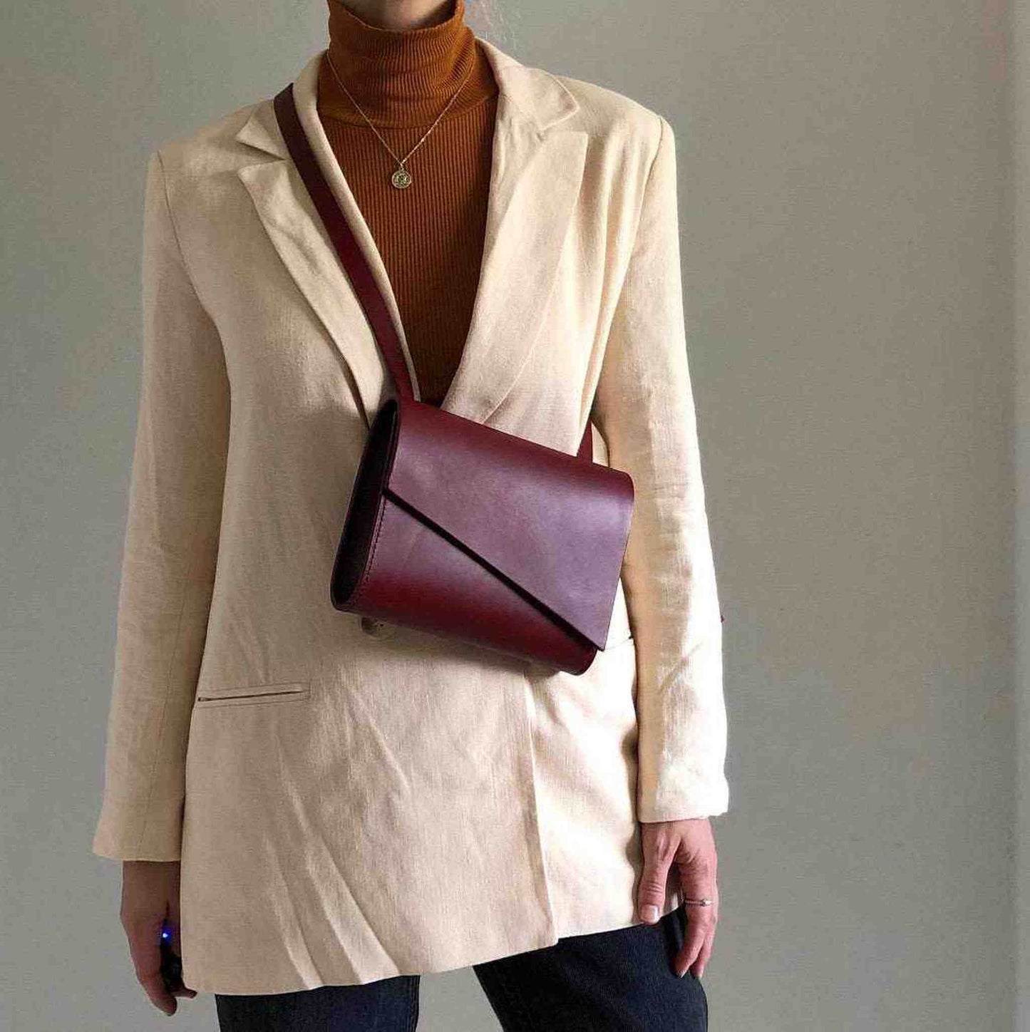 Red leather crossbody bag worn with a beige blazer; minimalist design with adjustable strap.