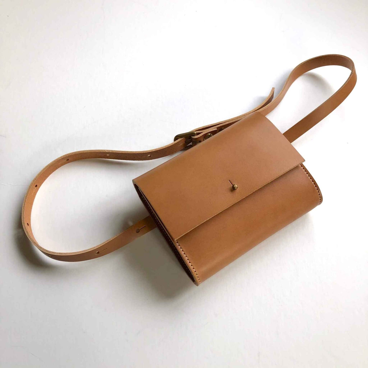 Tan leather belt bag with adjustable strap and squared flap, designed for versatile wear around the waist, crossbody, or over the shoulder.