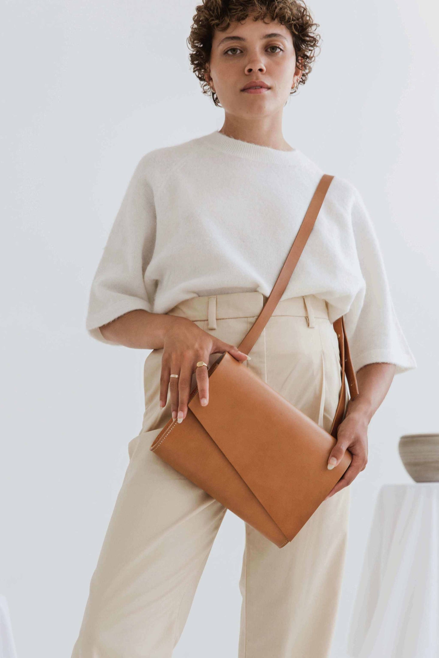 Tan leather crossbody bag worn by a model with an asymmetrical flap and adjustable strap.