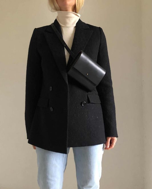 Sedna Black Leather Bum Bag worn crossbody on person wearing a black coat and light jeans.