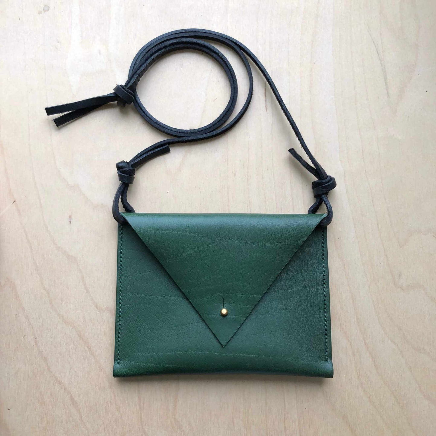 Drifter Mini Pocket Bag in green leather featuring a triangular flap and brass closure on a wooden background.