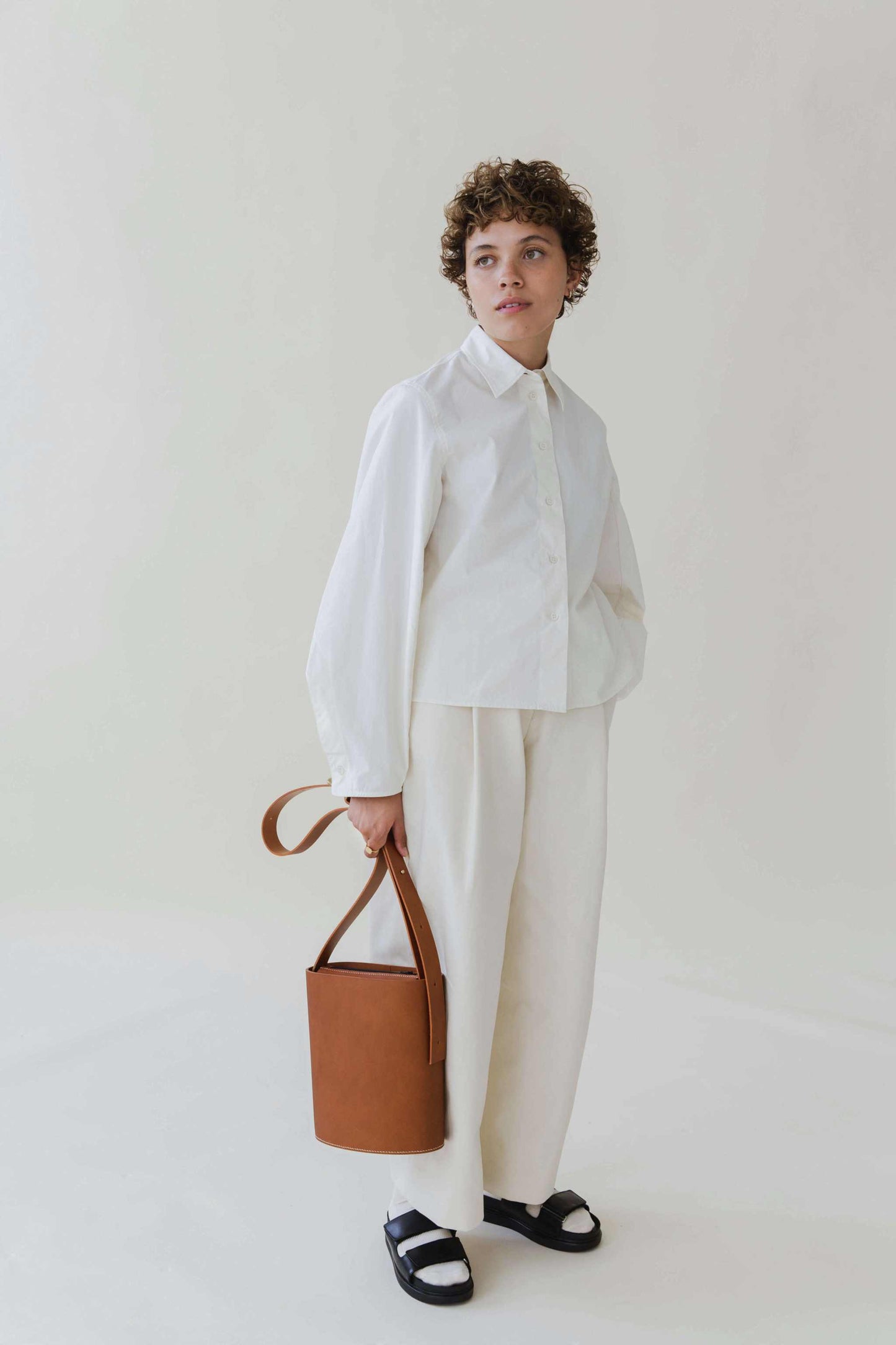 Oval Midi Leather Bag in tan, held by model wearing white outfit.