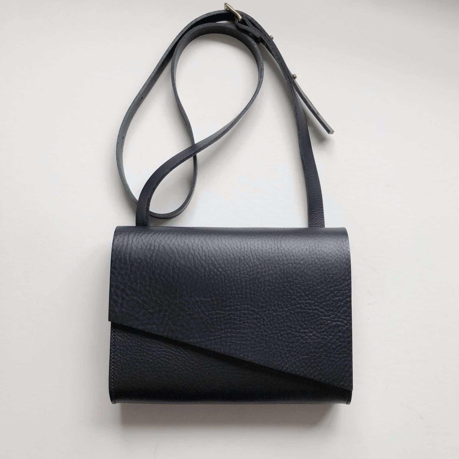 Black leather crossbody bag with asymmetrical flap and adjustable strap.