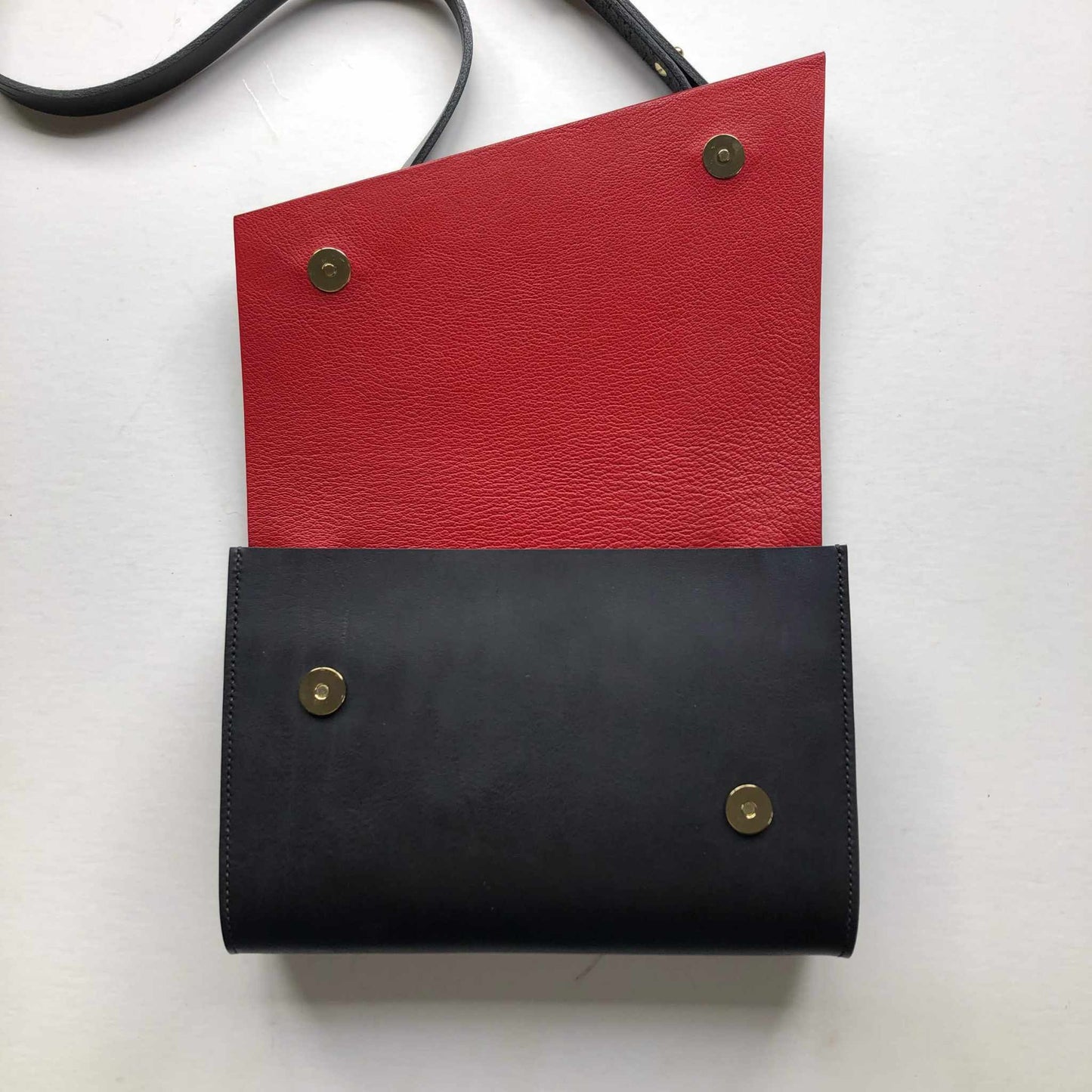 Pioneer Midi Black Leather Crossbody Bag with red interior flap, featuring asymmetrical design and brass button closure.