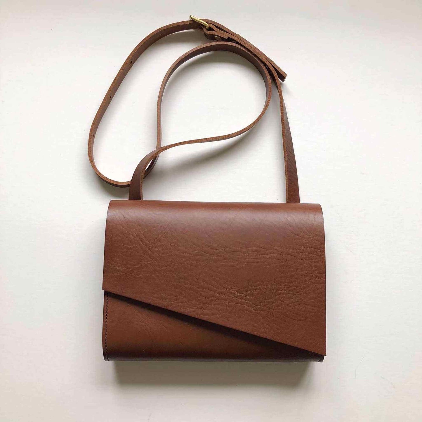 Tan leather crossbody bag with asymmetrical flap and adjustable strap.