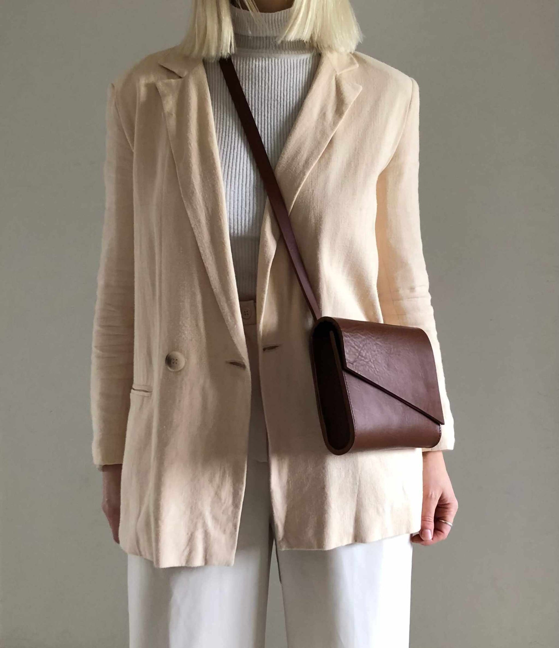 Tan leather crossbody bag with adjustable strap worn by woman in beige blazer.