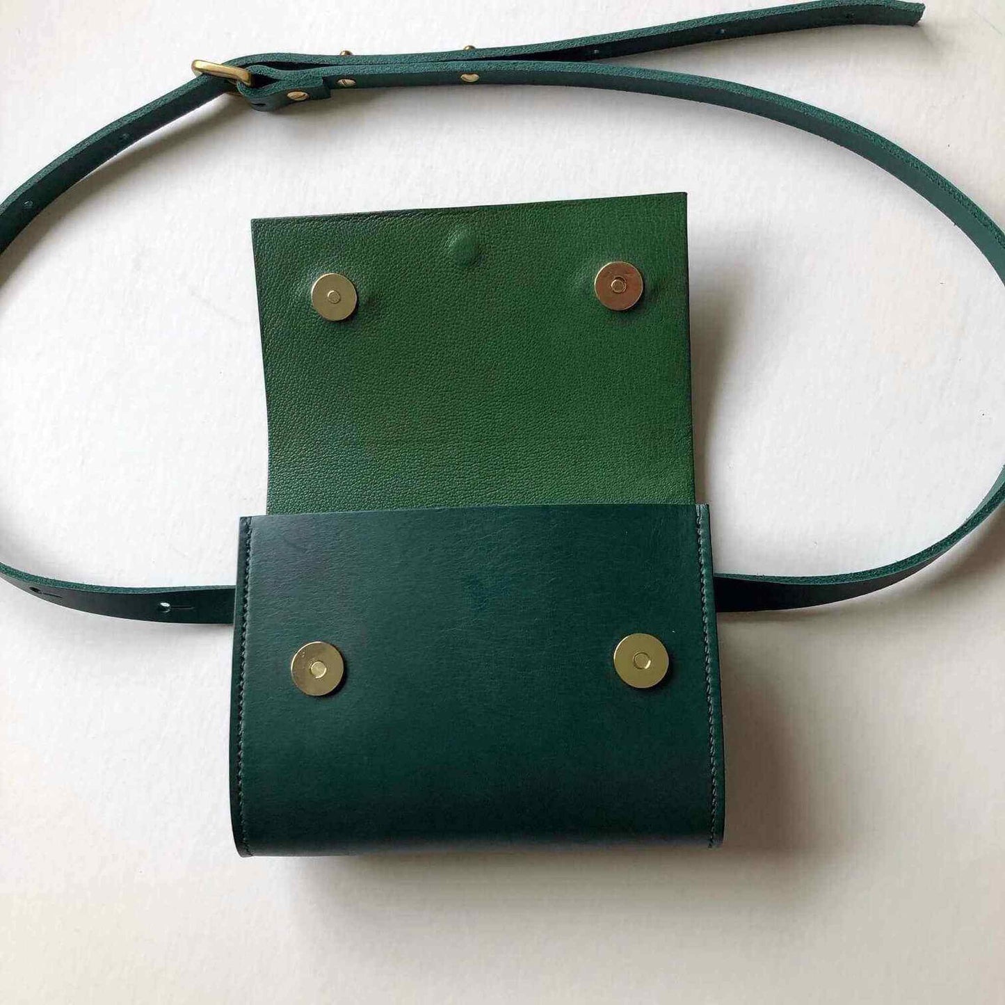 Green leather belt bag with adjustable strap and magnetic clasps.