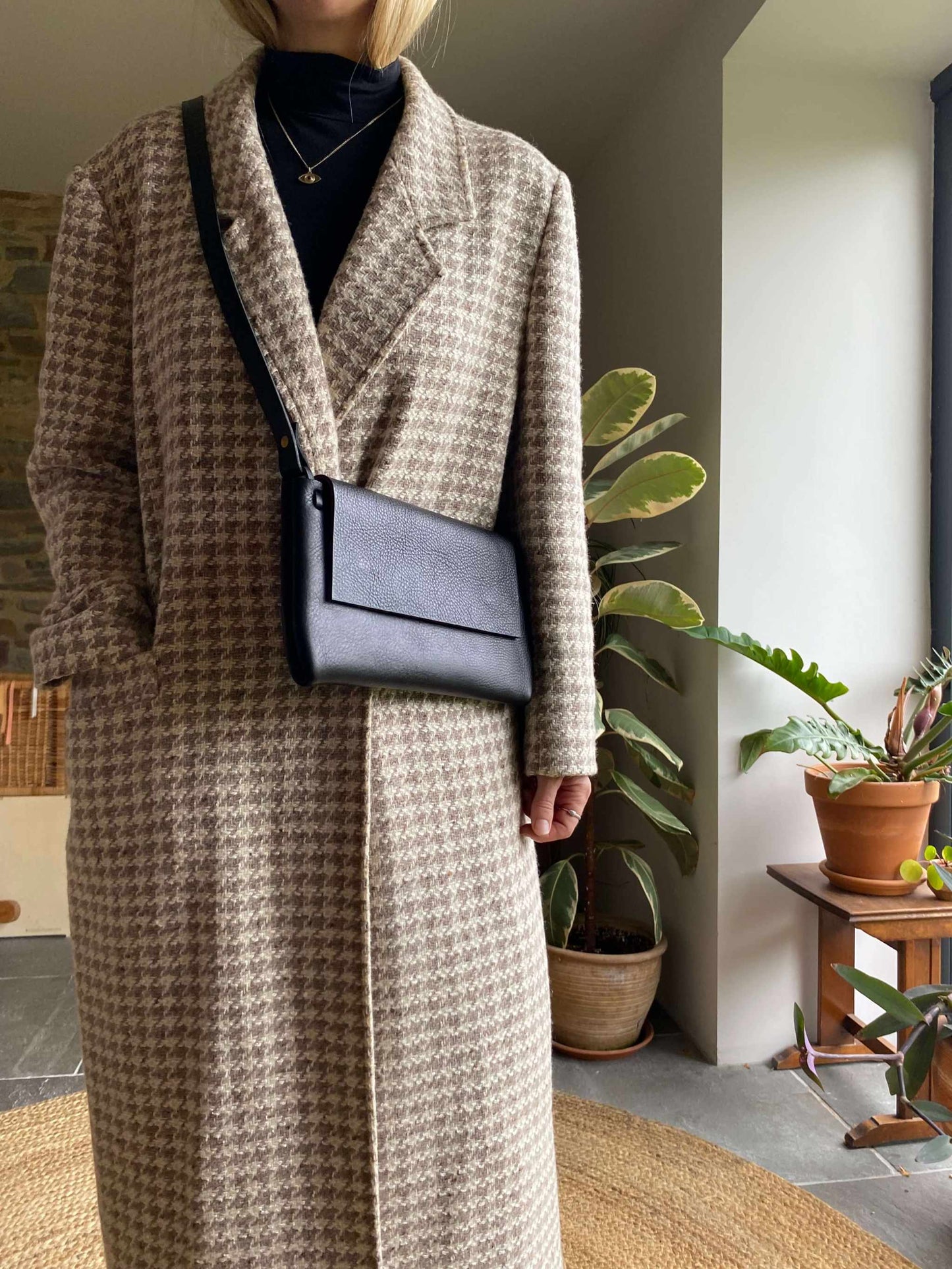 Minimalist fold leather crossbody bag in black worn over a coat.