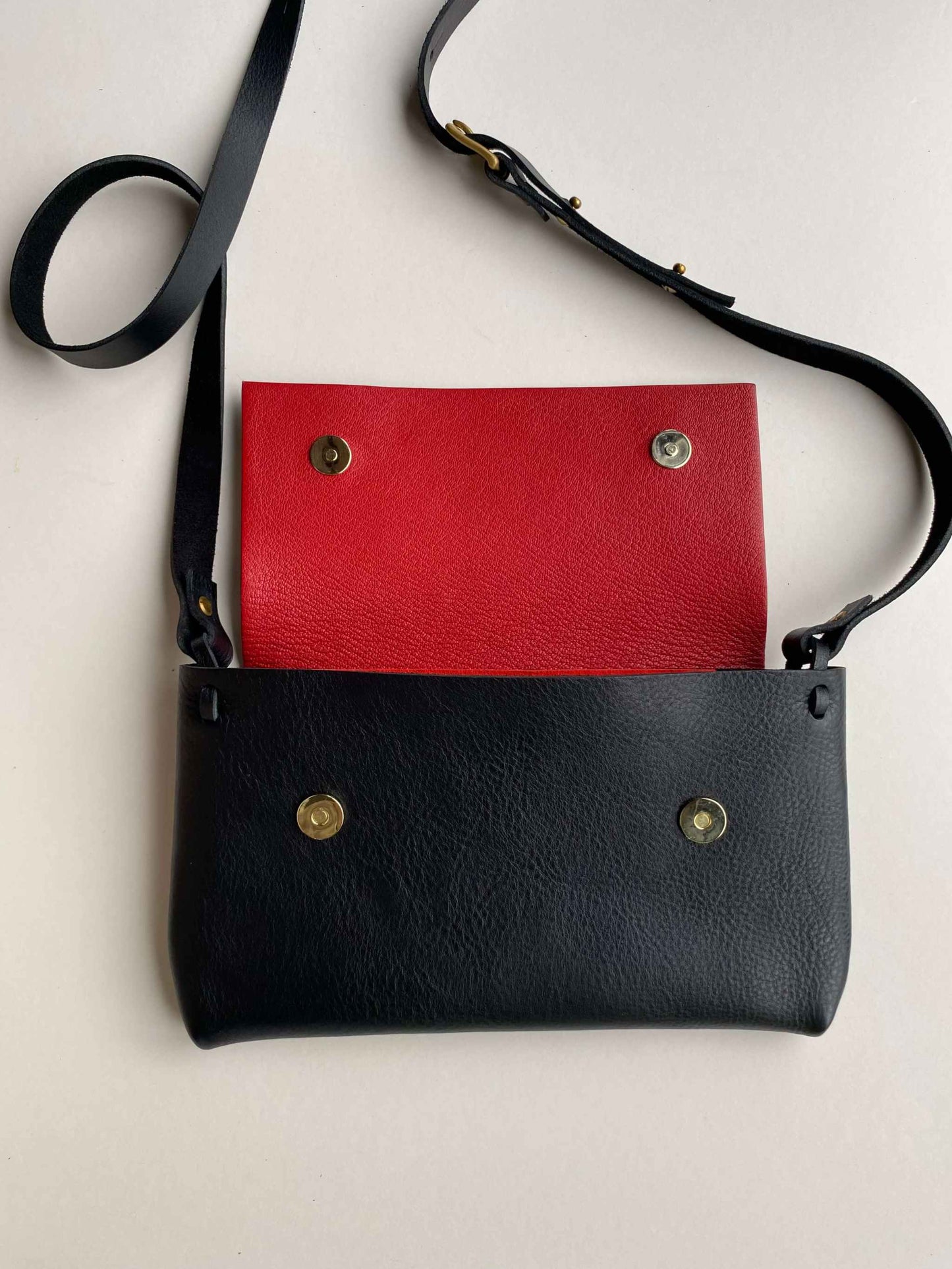 Fold Leather Crossbody Bag in black with red lining and adjustable strap.