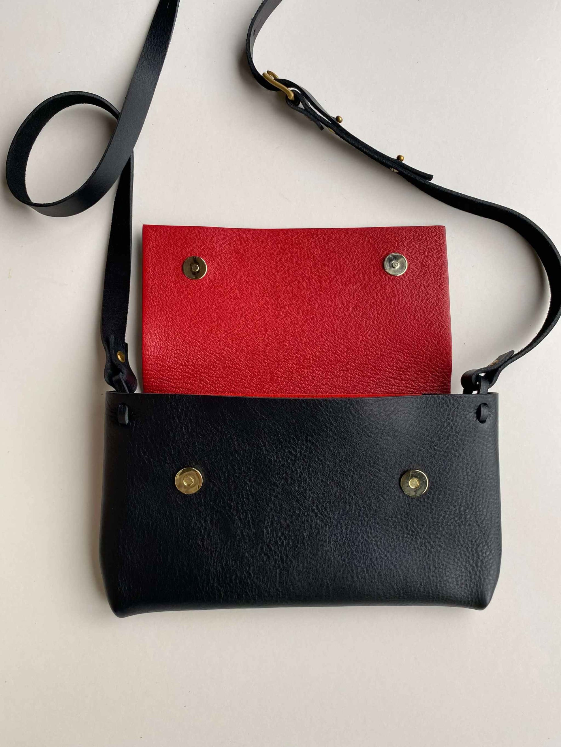 Fold Leather Crossbody Bag in black with red lining and adjustable strap.