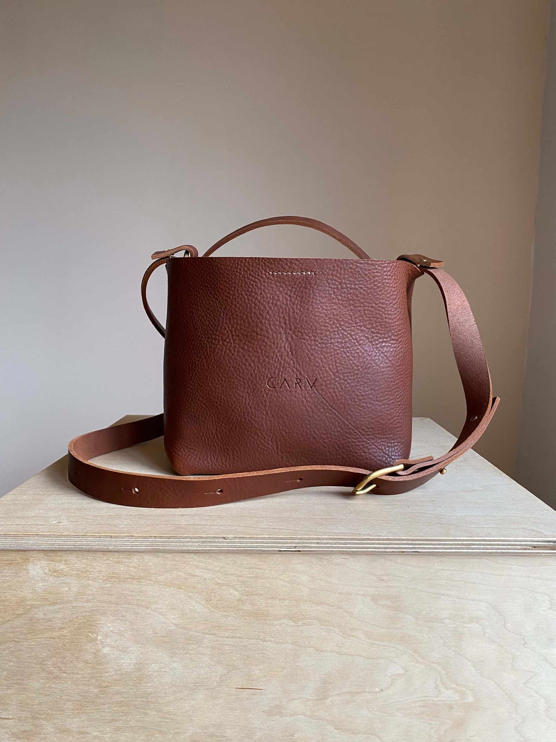 Basket Mini Leather Tote Bag in Tan on a wooden surface, featuring interchangeable straps.