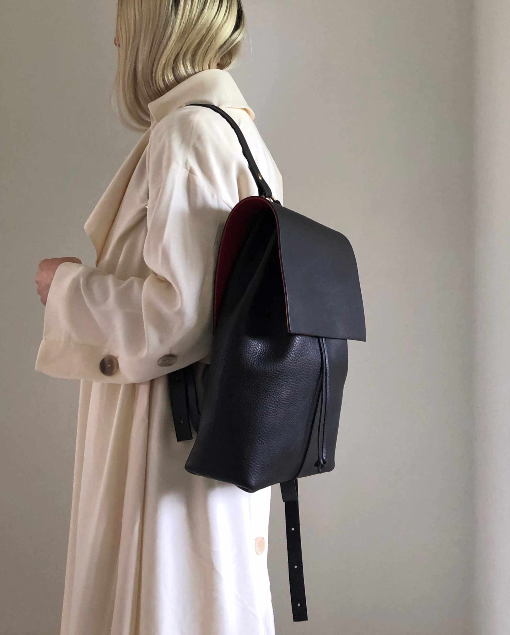 Tan leather backpack with squared flap design, worn by a person in a beige coat.