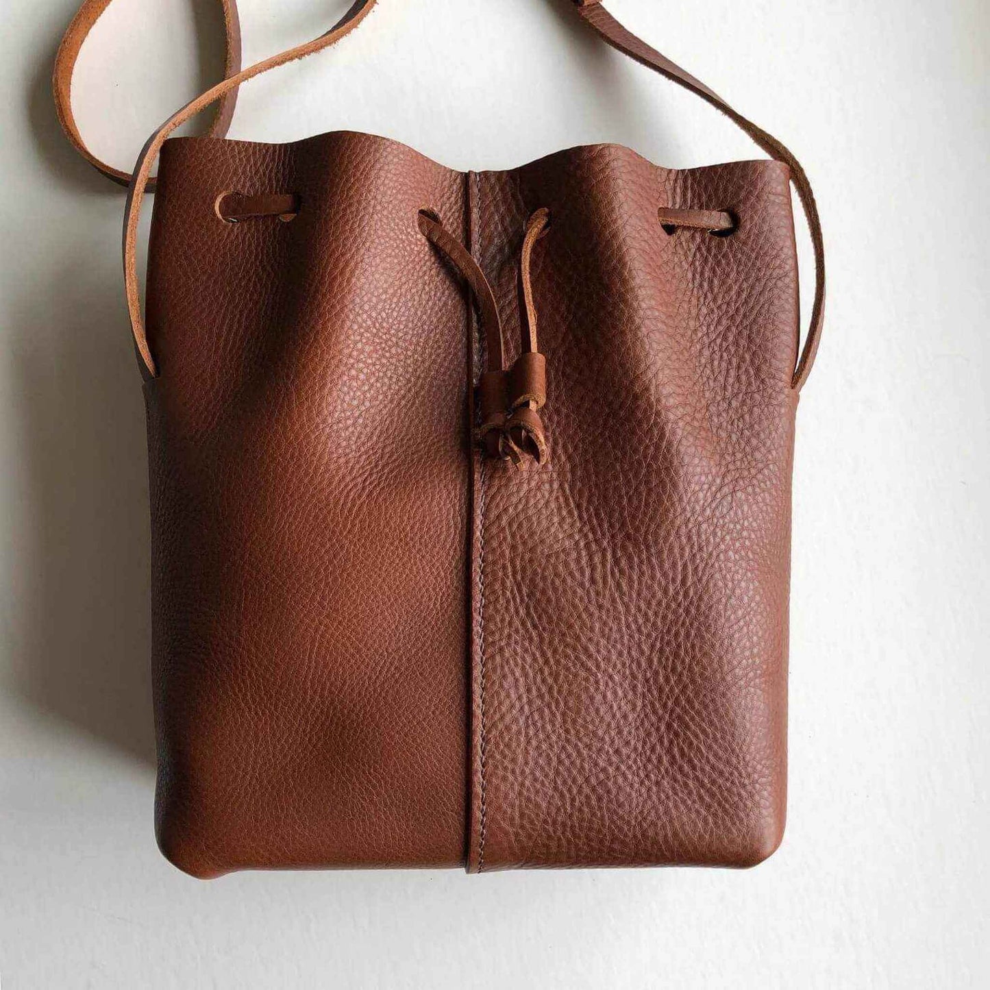 Nomad Midi Tan Leather Bucket Bag with drawstring design and adjustable strap.