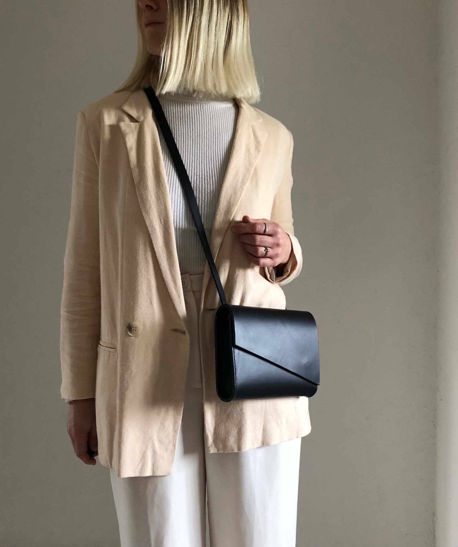 Pioneer Mini Black Leather Crossbody Bag worn with beige blazer, showcasing minimalist style and craftsmanship.