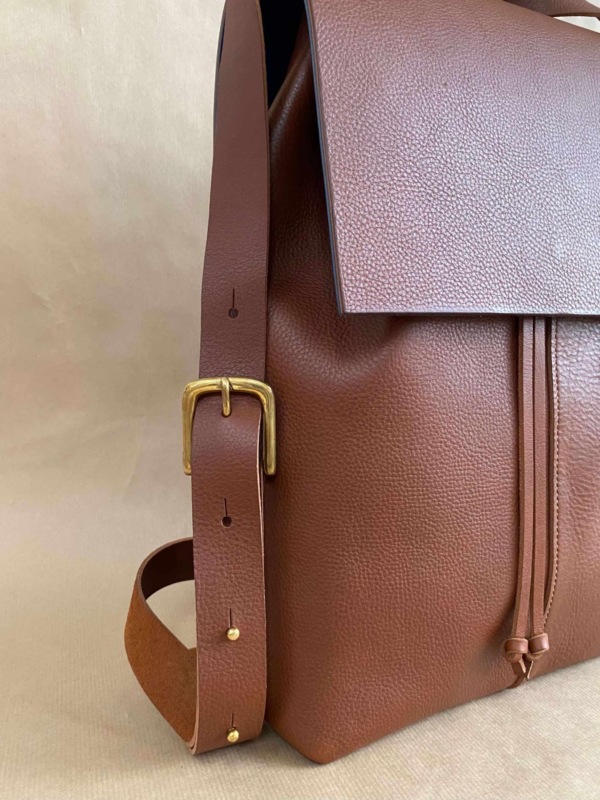 Tan leather backpack with squared flap design and adjustable straps.