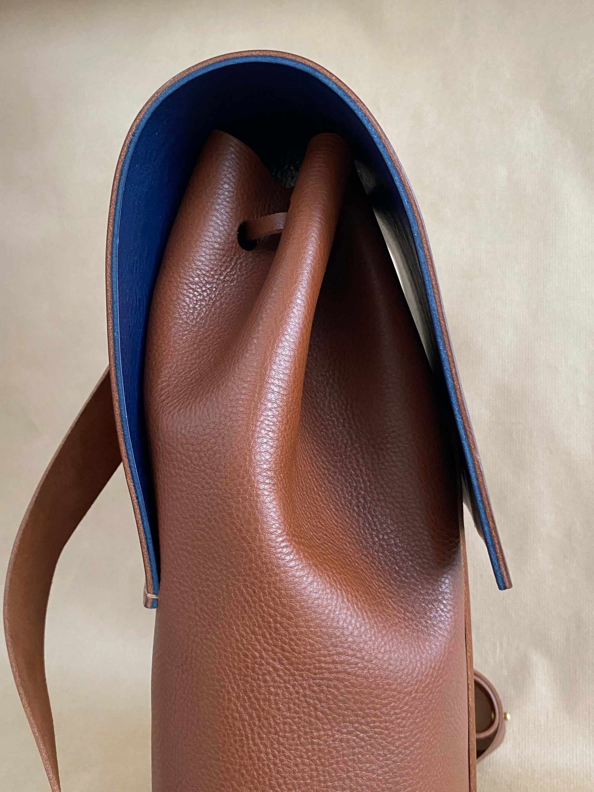 Tan leather backpack with a contemporary design and blue interior lining, featuring a minimalist style and sustainable craftsmanship.